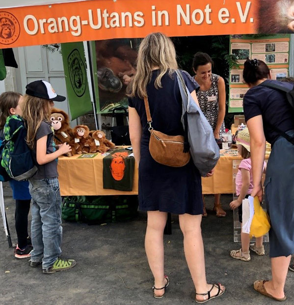 Erwachsene und Kinder stehen vor dem Infostand des Orang-Utans in Not e.V. Am rechten Bildrand steht eine Beachflag mit dem Vereinslogo.