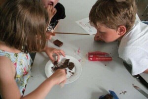 Zwei Kinder beim Workshop. Sie blicken gespannt auf ein Stück Schokolade.