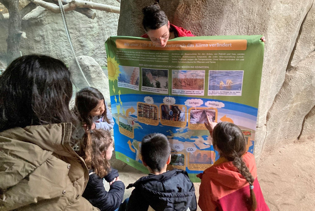 Kinder betrachten ein Plakat mit Informationen zum Klimawandel, das die Umweltbildnerin hochhält.