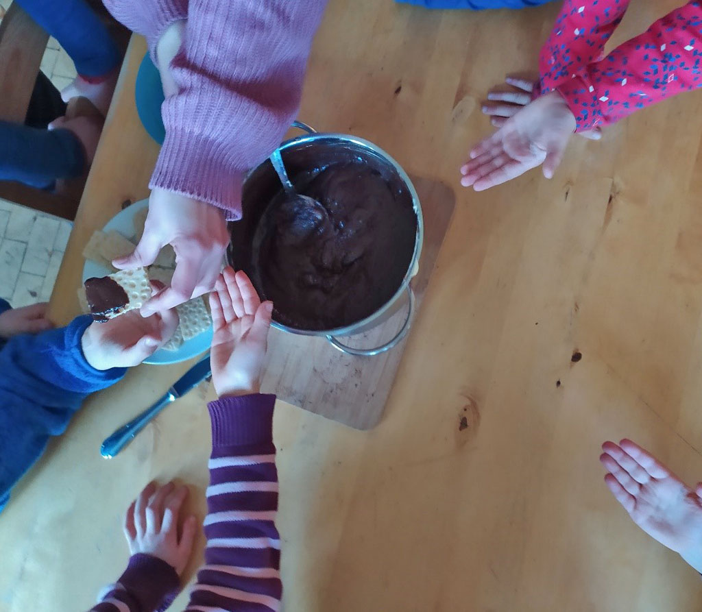 Nach der Zubereitung der Schokocreme halten die Kinder ihre Hände auf, um die mit Schokocreme bestrichenen Knäckebrotstücke zum Probieren zu erhalten.