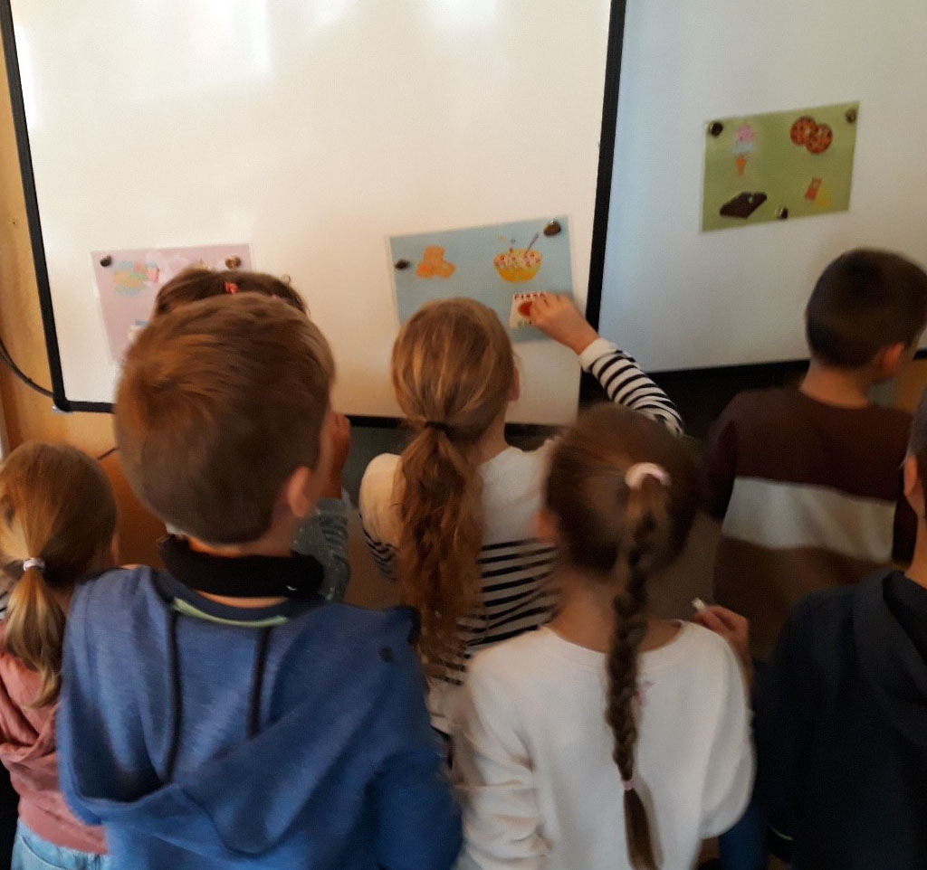 Mehrere Kinder stehen an einer Tafel, an der Bildkarten befestigt sind.