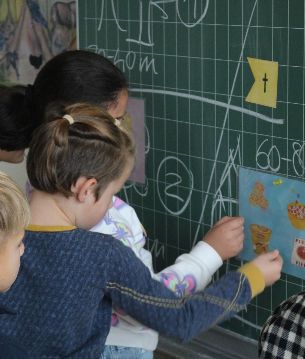 Mehrere Kinder stehen an einer Tafel. Daran sind Bildkarten befestigt.