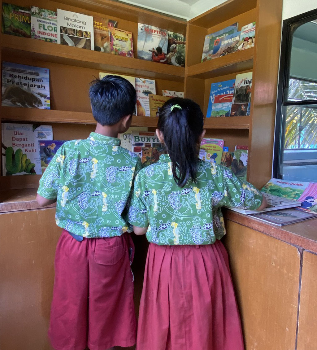 Zwei indonesische Schulkinder stehen im Bibliotheksbus und betrachten Bücher.